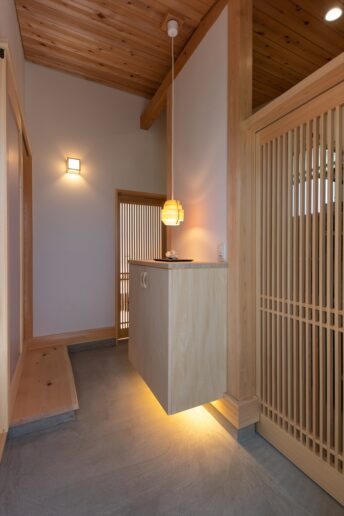 造作の千本格子建具が美しい玄関土間。右は収納、奥は趣味室に続いています。明るすぎない落ち着いた雰囲気になるように照明計画にこだわりました。