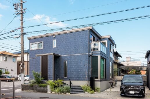 彫りの深いダークブルーの外観が上質な趣を漂わせる。
格子で玄関をさりげなく目隠しし、クランクした階段アプローチが動きのある景観を作り出す。