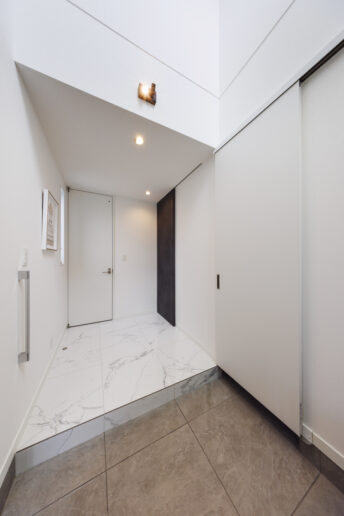 玄関ドアを開けた瞬間、誰もが歓声を上げる吹き抜けのエントランス。真っ白で統一し、より高級感を演出しています。右側の引き戸を開けるとシューズクローゼットからサニタリーへとつながります。