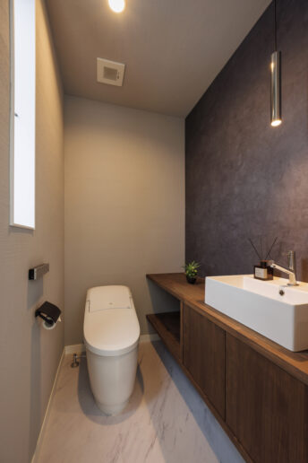 濃いグレージュのクロスがアクセントのスタイリッシュなトイレ。デザイン性だけでなく、大容量の収納棚を造作して実用性も高めています
