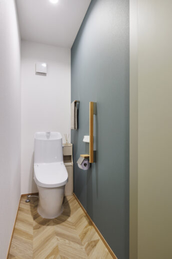 やわらかな色合いと自然素材を取り入れた、北欧テイストのトイレ。落ち着いたブルーグリーンのアクセントクロスが空間に彩りを添え、木目の質感があたたかみをプラスしています。