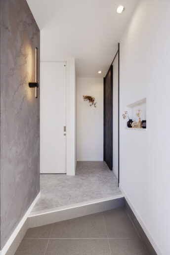 白とグレーで構成された玄関ホール。シューズクローゼットとの境目となる壁にアーティスティックなイタリア漆喰「ユーロスタッコ」を塗ってアクセントをつけました。