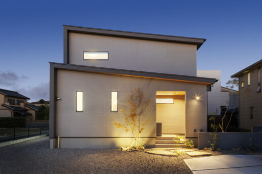 ライトグレーのALCと深めの軒がバランス良く融合した外観。日が暮れると、シンボルツリーが美しくライトアップされます。窓を少なめにしてプライバシーを守り、リビングの吹き抜けから自然光を取り込む設計手法を採用しました。